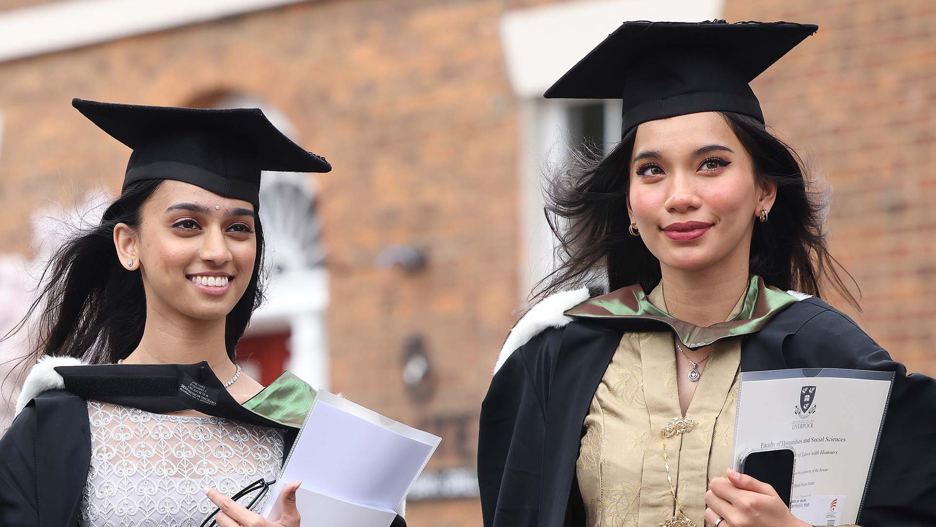 Two graduates holding their degree certificates