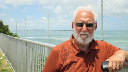 man in orange shirt standing with bridge in the background