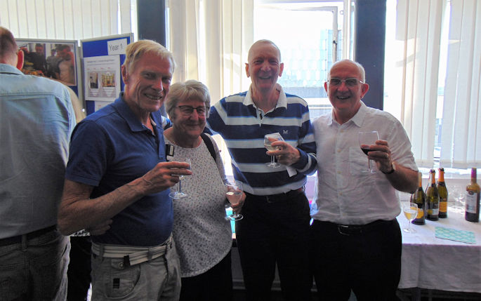 Four people stand together holding drinks and smiling