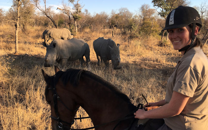 Alumna Danielle Jackson on horseback in the South African outback overlooking two rhinos