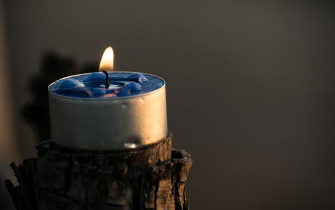 A lit tealight candle sits to the left of the image with thoughtful tonal blues surrounding it in the background