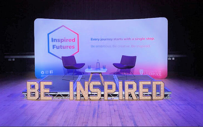 A stage with two purple chairs and large lights at the front saying Be Inspired
