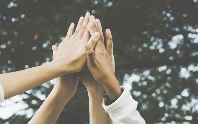 A picture of 4 hands coming together in a high five in the air