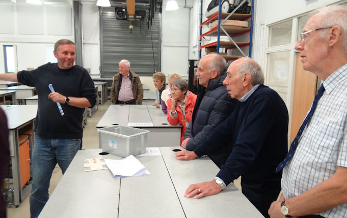 A group of alumni around a table being shown something by an academic