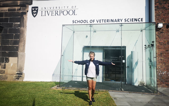Nicole Regan stands with her arms raised in the air in celebration outside the Veterinary Science building on the central Liverpool campus