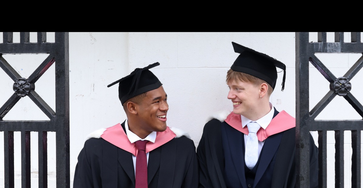 Two graduates in academic dress smile at each other