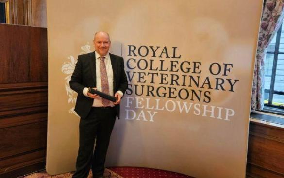 Adam smiling, standing in front of the RCVS board with his award