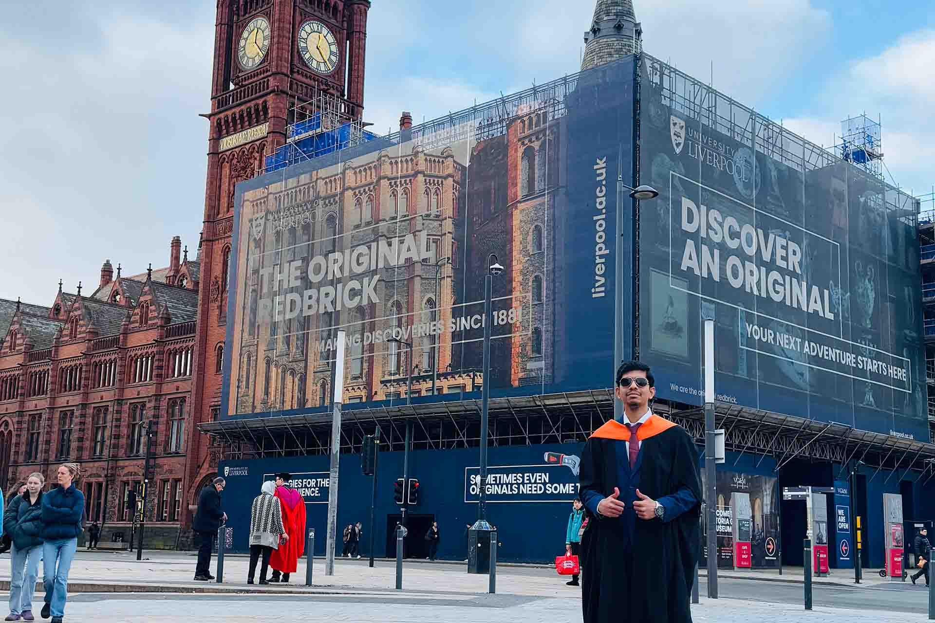 graduate in academic dress in front of a red brick building