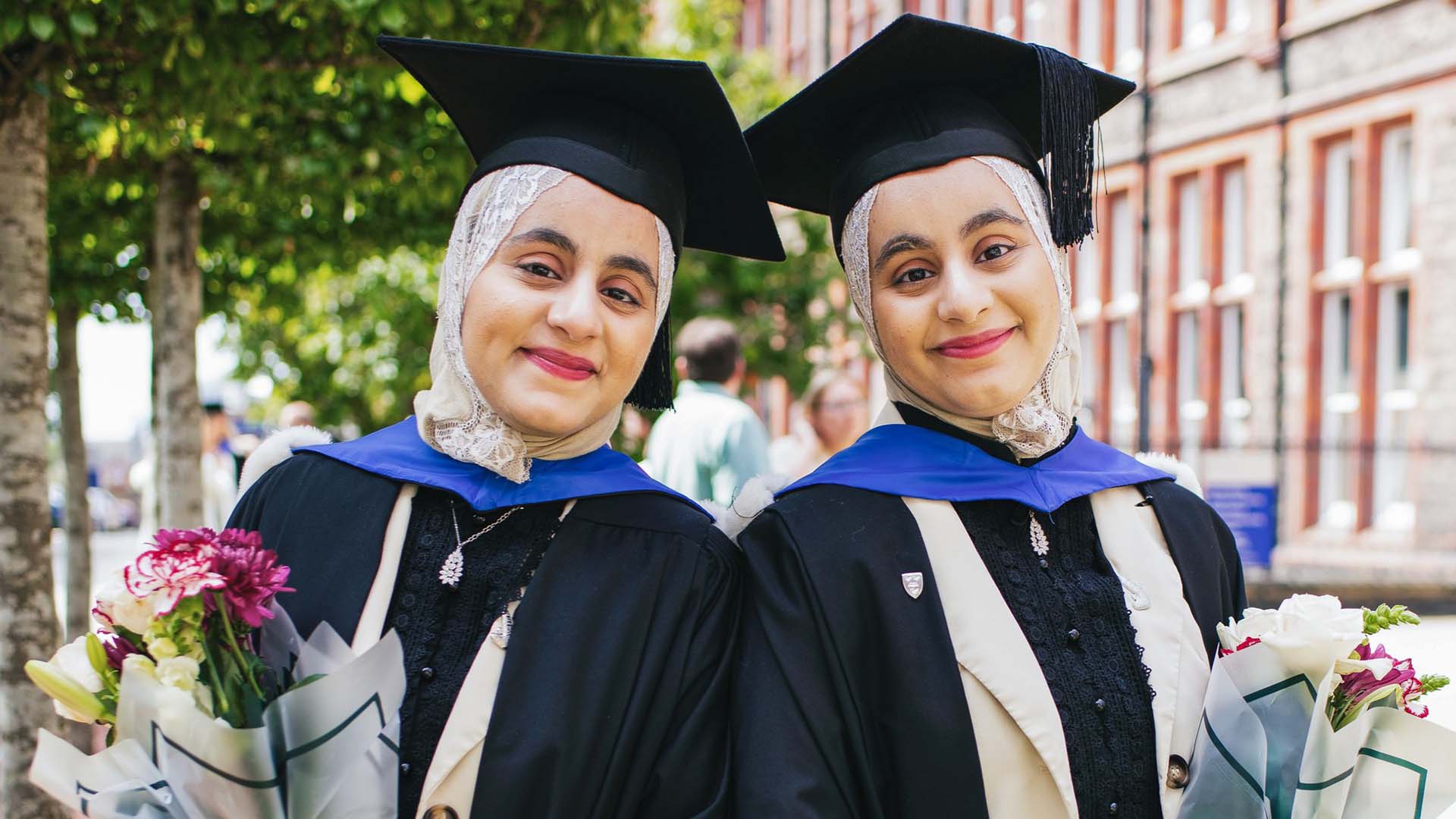 Two graduates pose for a photo with flowers in their hands