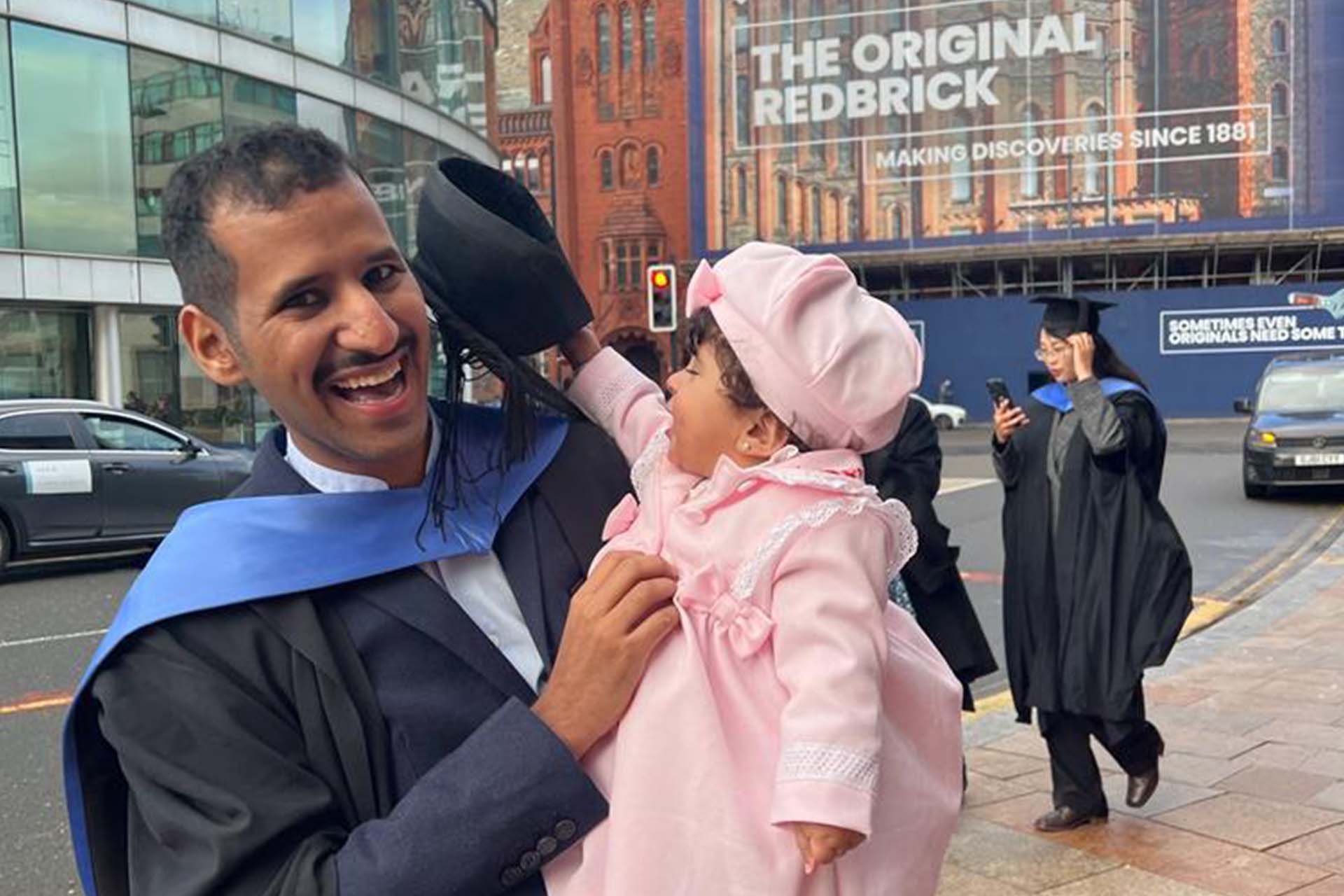 graduate in academic dress holding a child