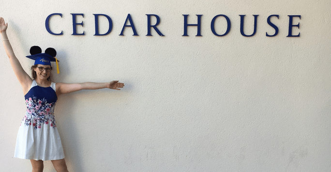 Kaylea posing with her graduation cap and Mickey Mouse ears next to the Cedar House sign