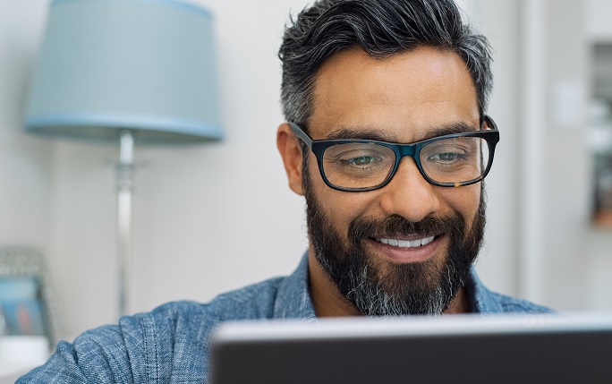 A man smiles whilst looking at laptop