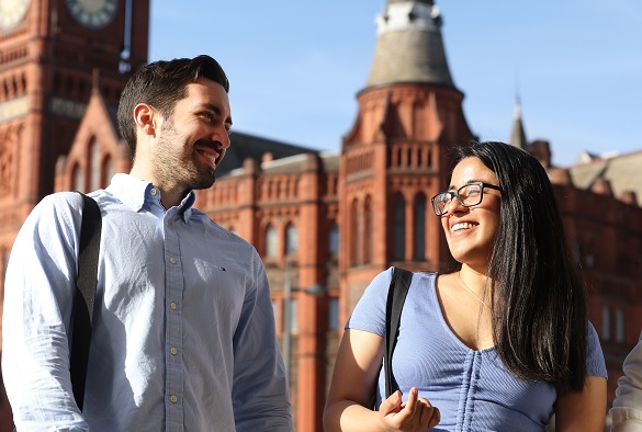 Two postgraduate students walk through University Square laughing and talking with the Victoria Building behind them