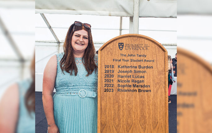 Rhiannon posing next to the John Tandy Final Year Student Award board
