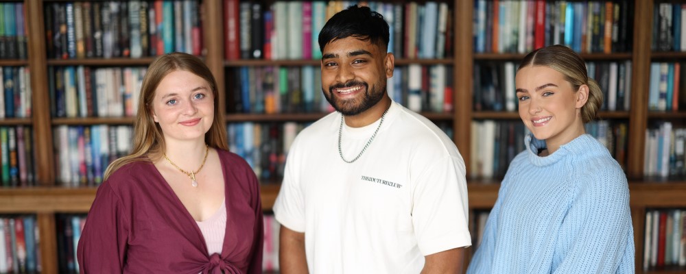 Three students standing in front of a bookcase