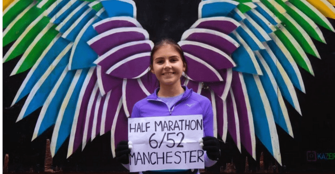 marathon runner holding sign in front of mural with angel wings